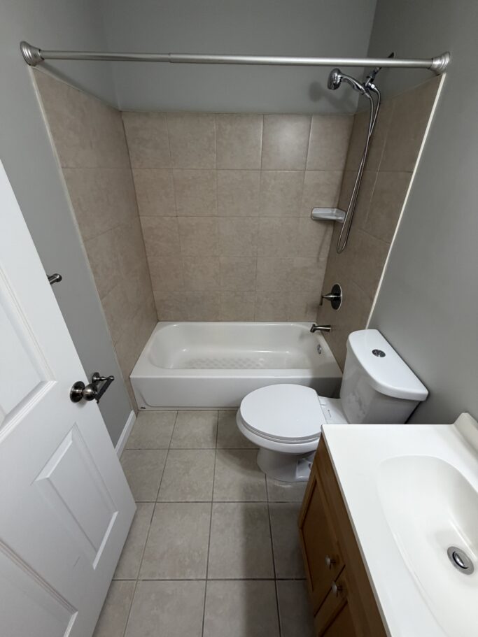 Bathroom featuring a shower-tub combination with beige tile walls, a white toilet, and a wooden vanity with a white sink.