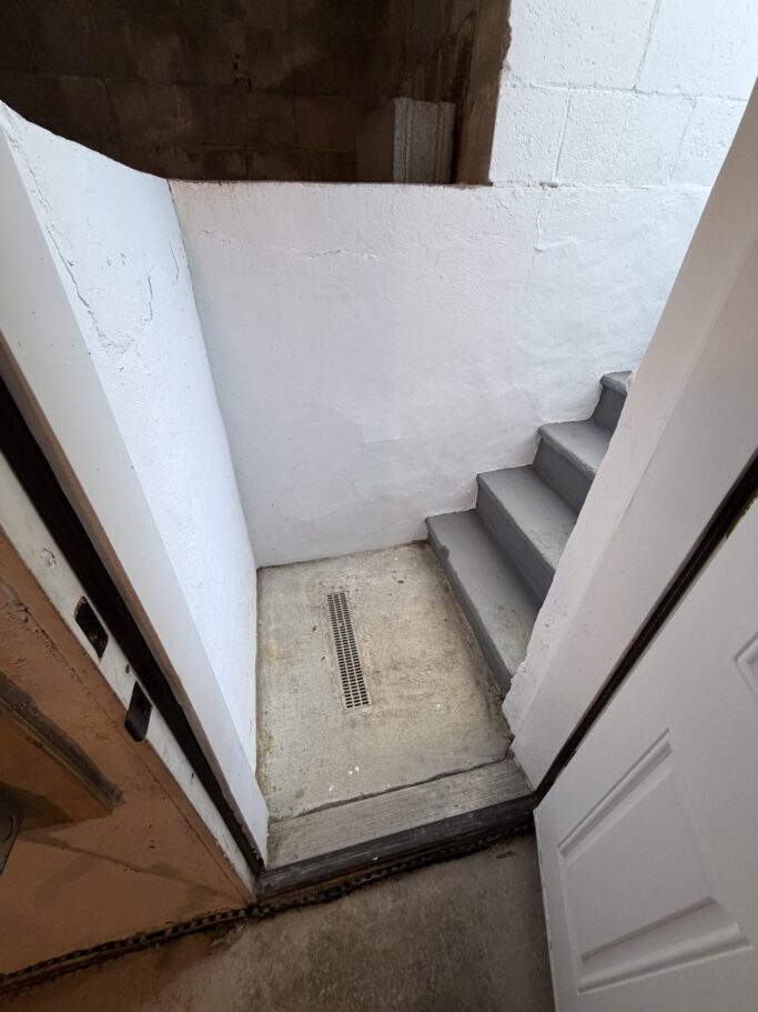 Concrete stairs leading up from a basement landing with a central floor drain.