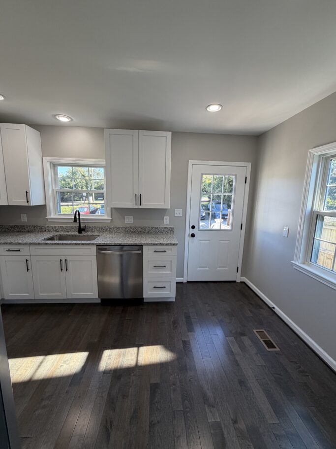 Kitchen with white cabinets, speckled countertops, a stainless steel dishwasher, and dark wood floors.
