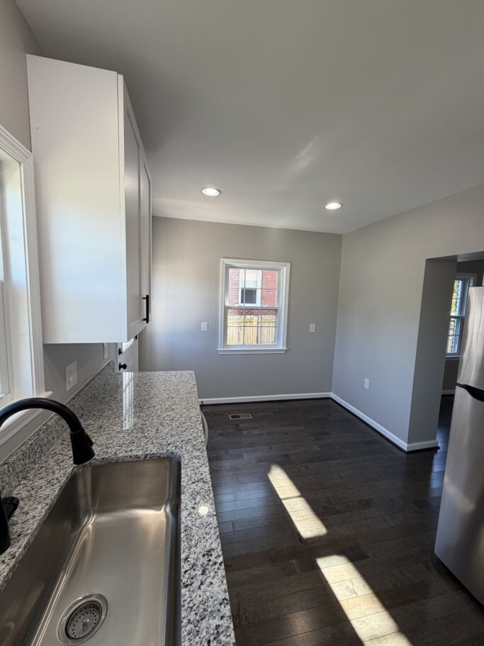 Kitchen view showing a stainless steel sink with a black faucet, granite countertops, white cabinets, and dark hardwood floors.