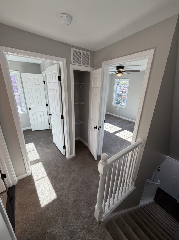 Hallway view showing two bedrooms, a small utility closet, and a staircase leading down.